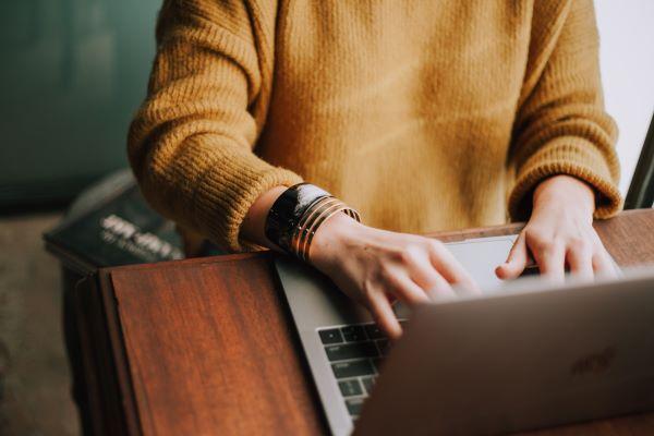 A woman in a yellow top typing on a laptop